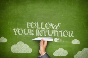 Follow your intuition concept on green blackboard with businessman hand holding paper plane