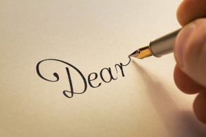 amintro amintro Hand is writing calligraphic letter starting with dear using old pen on yellow paper